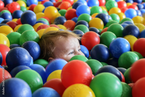 happy little child plays on a playground filled with colorful plastic balls.