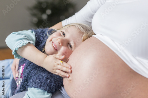 Glückliches Mädchen umarmt Babybauch der Mutter