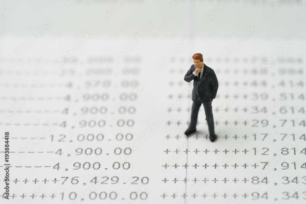 Growth of investment, interest compound in savings concept, miniature business man standing and thinking on numbers of money printed on paper bank account book Growth of investment, interest compound in savings concept, miniature business man standing and thinking on numbers of money printed on paper bank account book