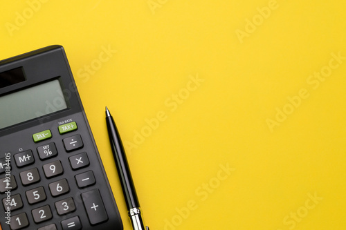 Flat lay or top view of black pen with calculator on vivid yellow background table with blank copy space, math, cost, tax or investment calculation