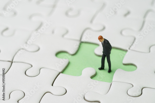 Finding the missing piece for business success concept, miniature people businessman standing and looking at the missing white jigsaw puzzle piece on pastel green background