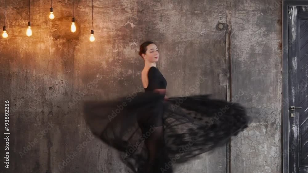 Attractive female dancer dancing and spinning indoor in the studio. Yellow lighbulbs handing on the wall. Girl dressed in a black tutu. Attractive female dancer dancing and spinning indoor in the studio. Yellow lighbulbs handing on the wall. Girl dressed in a black tutu.