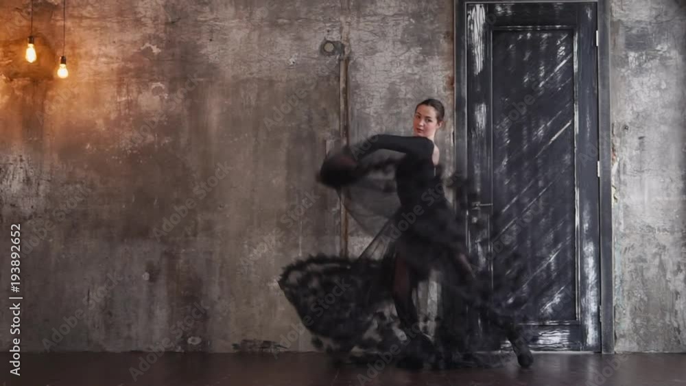 Charming brunette woman in long black dress does a show in a studio alone. She is dancing holding parts of dress. Charming brunette woman in long black dress does a show in a studio alone. She is dancing holding parts of dress.
