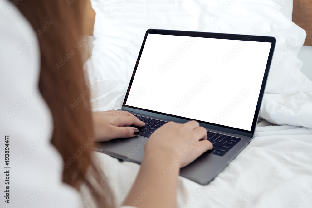 Fototapeta premium Makieta obrazu kobiety siedzącej na łóżku, używania i pisania na laptopie z pustą białą klawiaturą na ekranie