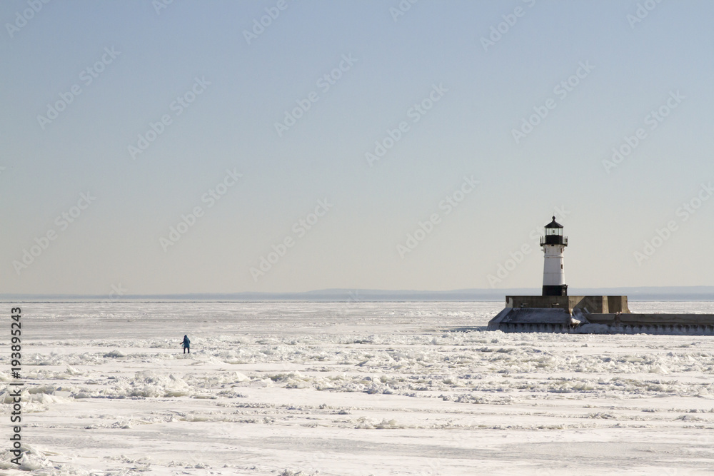 Person walkingon frozen Lake Superior along pier with lighthouse in Duluth, Minnesota