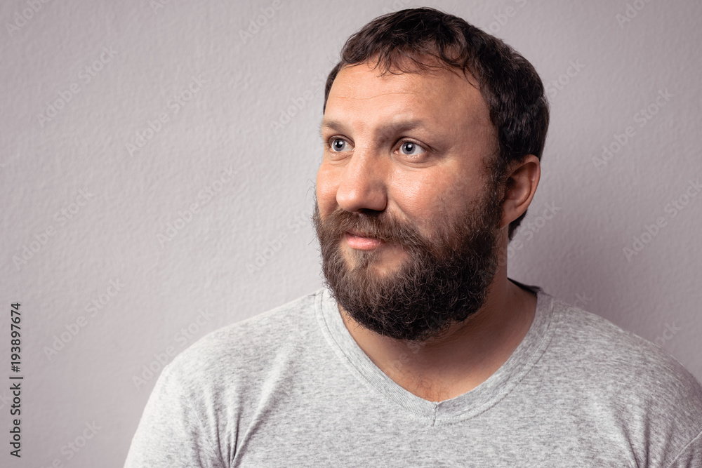 Fototapeta premium Happy bearded man in gray t-shirt looking away while standing against gray wall.