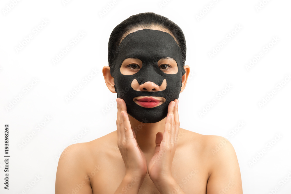 Young woman doing facial black mask sheet with purifying mask on her face on white background Young woman doing facial black mask sheet with purifying mask on her face on white background
