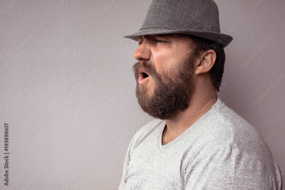 Side portrait of a bearded man shouting. Portrait of bearded angry man against a gray wall. Anger, rage. Side portrait of a bearded man shouting. Portrait of bearded angry man against a gray wall. Anger, rage.
