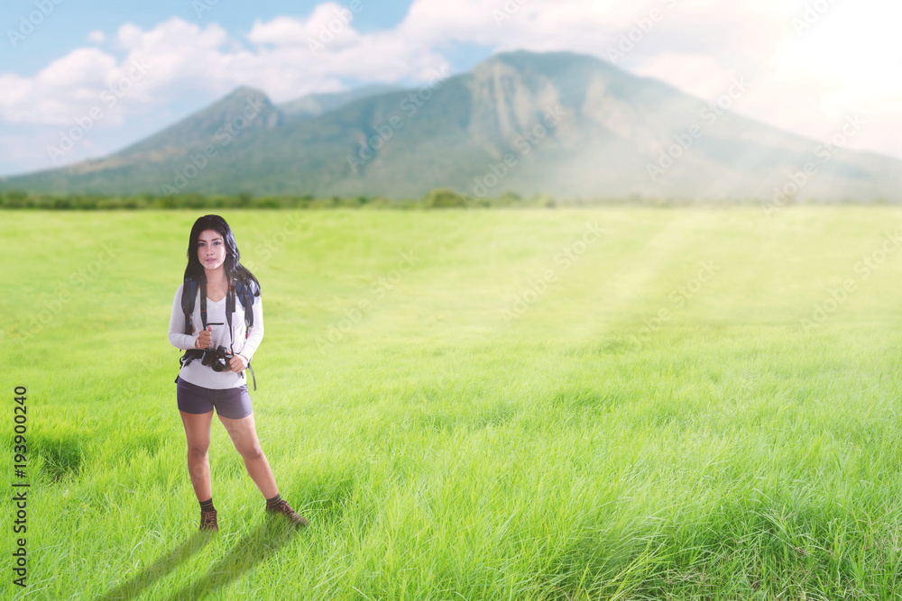 Asian tourist woman walking on a greenery hill trail with backpack and camera