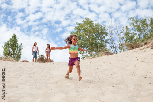 Happy Smiling girl running down the dunes at the beach while her sisters look on. © soupstock