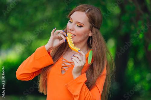 Portrait of pretty red hair woman with juicy delicious orange at summer green park.