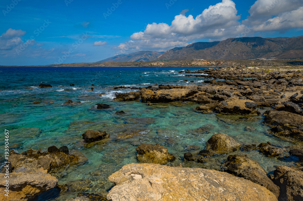 the rocky shore of the sea. the turquoise sea and mountains on a blue sky background with clouds. Elafonisi, Crete, Greece