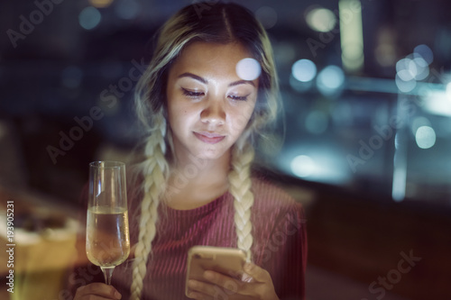 Serious young woman using a smartphone at a rooftop bar in the evening