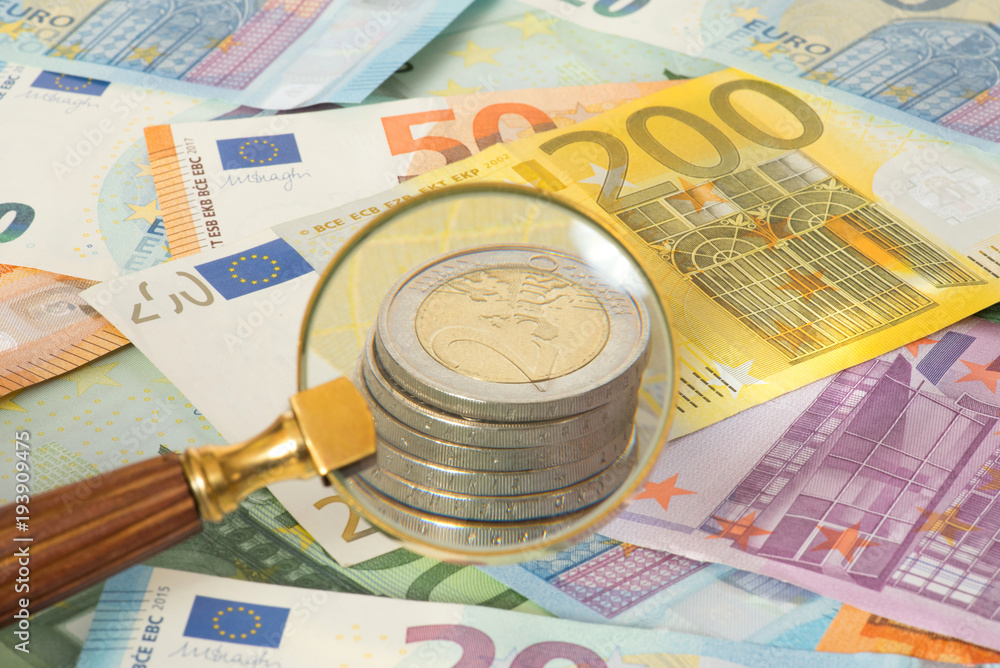 Eine Lupe, Euro Geldscheine und Euro Münzen Eine Lupe, Euro Geldscheine und Euro Münzen