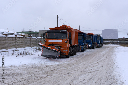A column of five snow-remover trucks on the road in winter during a snowfall .