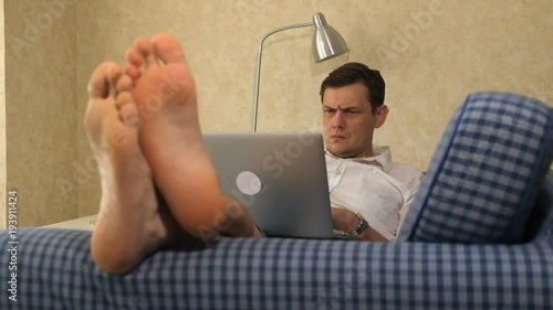 serious business man lying on sofa, working with laptop, pensive. feet, close-up photo