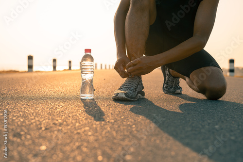 Male runner tying shoes in preparation for a run in the morning and bottle water. The concept of health and fitness