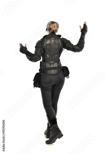 full length portrait of female soldier wearing black tactical armour facing away from camera, isolated on white studio background.