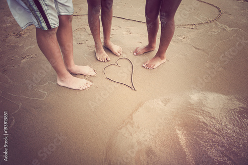 Racially diverse children's feet at the beach with a heart drawn in the sand photo