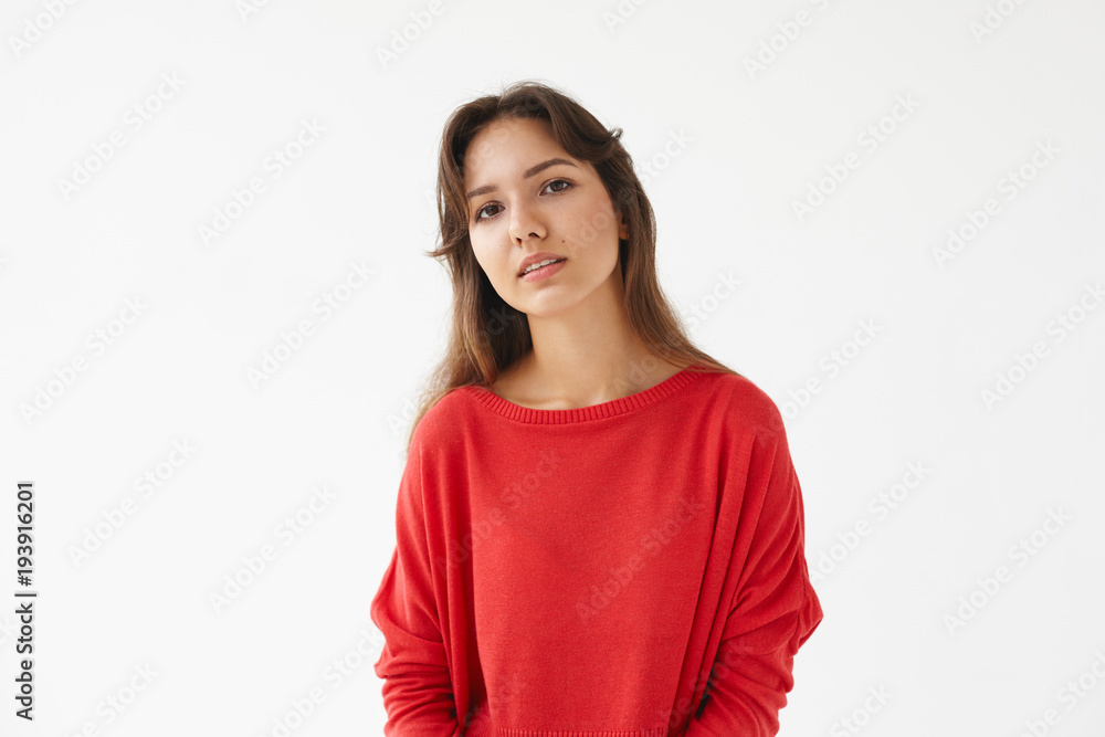 Horizontal isolated shot of serious beautiful young mixed race woman with brown hair posing in studio dressed in red oversize long sleeved top, looking at camera with calm facial expression Horizontal isolated shot of serious beautiful young mixed race woman with brown hair posing in studio dressed in red oversize long sleeved top, looking at camera with calm facial expression