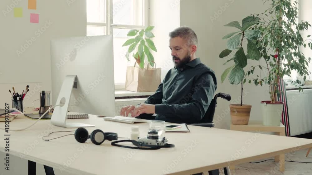 Businessman in wheelchair at the desk in his office. Businessman in wheelchair at the desk in his office.
