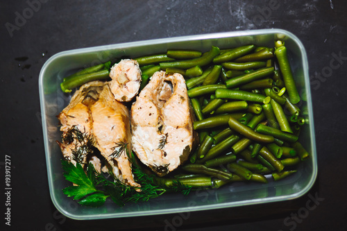 Healthy snack, food in a container. Baked red fish, pink salmon, salmon and green beans on black background close up.