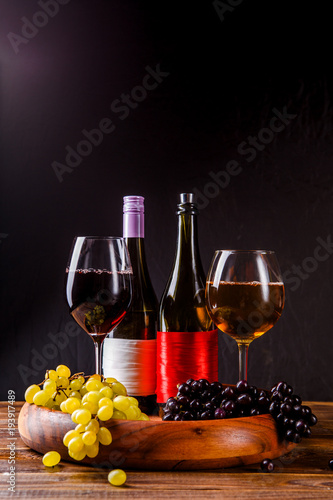 Picture of wine glass with wine, grape black, green on wooden tray on table