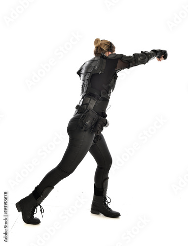 full length portrait of female soldier wearing black tactical armour facing away from camera, isolated on white studio background.