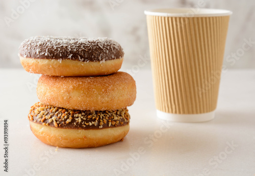 Paper cup of coffee with tasty donuts on white background.