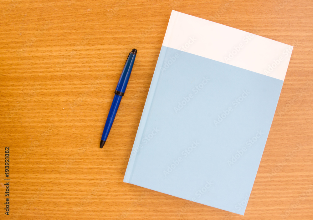Hardcover book with ballpen on wooden table, top view shot. Hardcover book with ballpen on wooden table, top view shot.