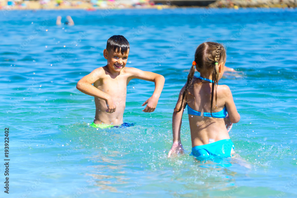 Little boy and girl playing splashing sea water on beach holiday
