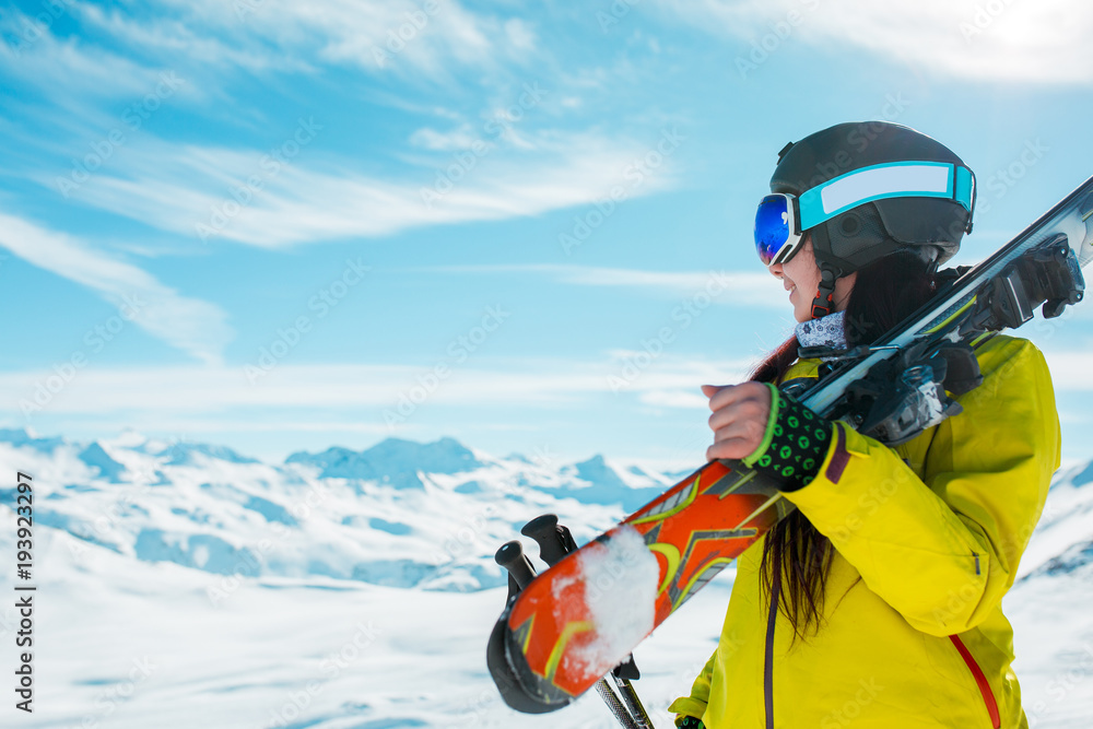 Photo of side view of sporty woman in helmet with skis on her shoulder against background of winter hills Photo of side view of sporty woman in helmet with skis on her shoulder against background of winter hills