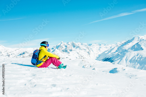 Photo of sports woman wearing helmet and mask sits on snowy slope