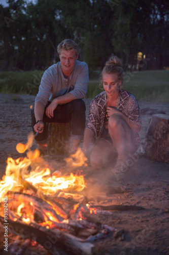 Boy and girl roasting marshmallows over a campfire at dusk