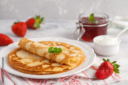 Thin hot pancakes with cottage cheese, jam and strawberries. Healthy traditional breakfast concept.