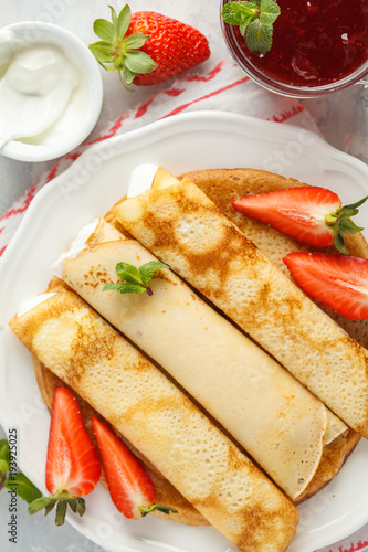 Thin hot pancakes with sour cream, jam and strawberries. Top view, copy space. Healthy traditional breakfast concept.