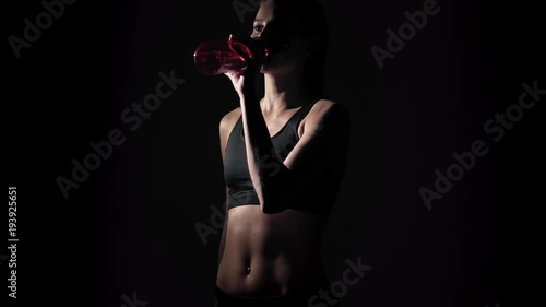 Slim young woman drinking water after training a on a black background. belly sports girl close-up photo