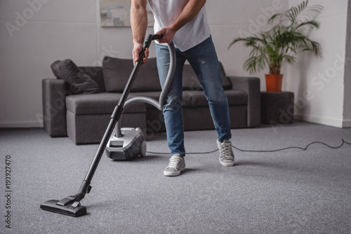 cropped image of man cleaning living room with vacuum cleaner
