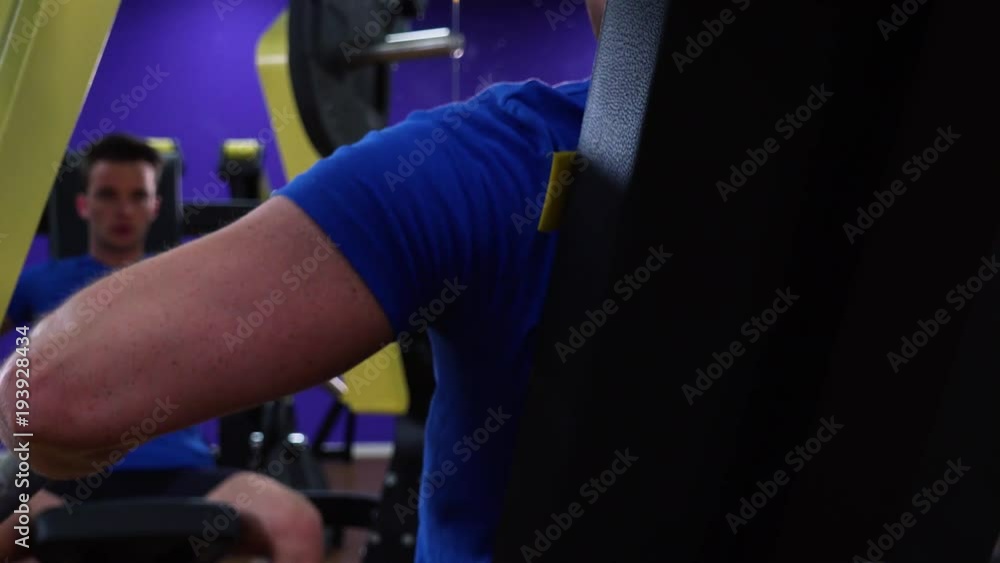 A fit man trains on a machine in a gym - closeup from behind A fit man trains on a machine in a gym - closeup from behind
