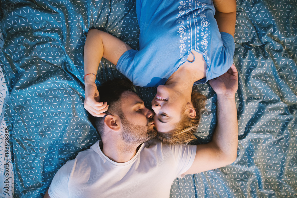 Cheerful happy romantic couple lying on the bed with bodies in opposite  ways while cuddling and kissing. Relationship and weekend goals. Stock  Photo | Adobe Stock