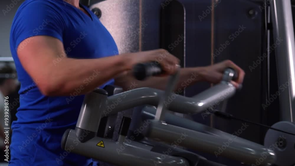 A fit man trains on a machine in a gym - closeup on the torso from the side A fit man trains on a machine in a gym - closeup on the torso from the side