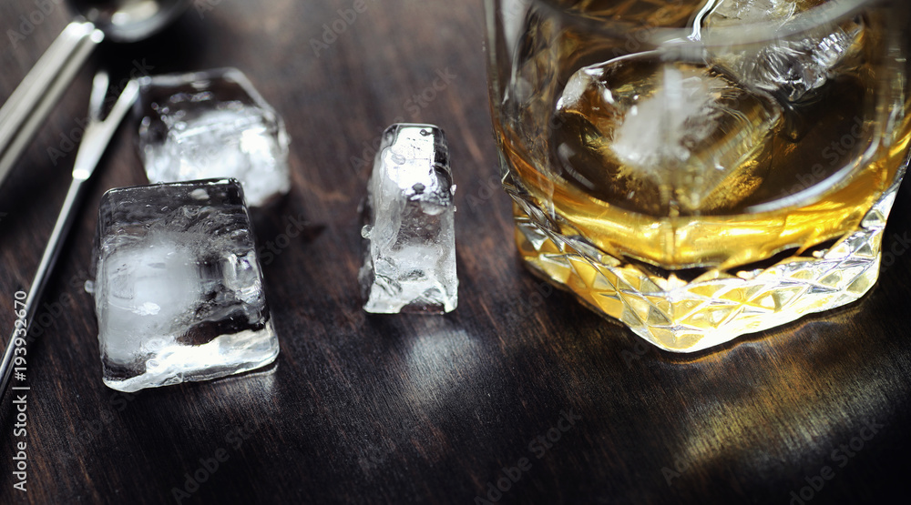 Whiskey with ice with a glass. Cubes of ice on a wooden table an Whiskey with ice with a glass. Cubes of ice on a wooden table an