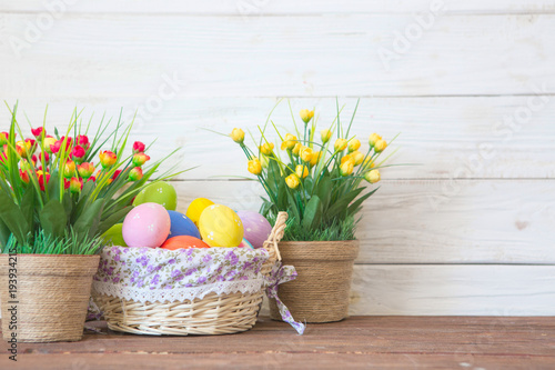 Colored easter eggs in the basket and spring flowers on wooden background. Greeting card