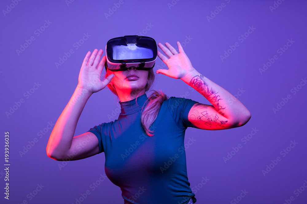 Tattoed sexy woman wearing a virtual reality VR head set on blue background Tattoed sexy woman wearing a virtual reality VR head set on blue background