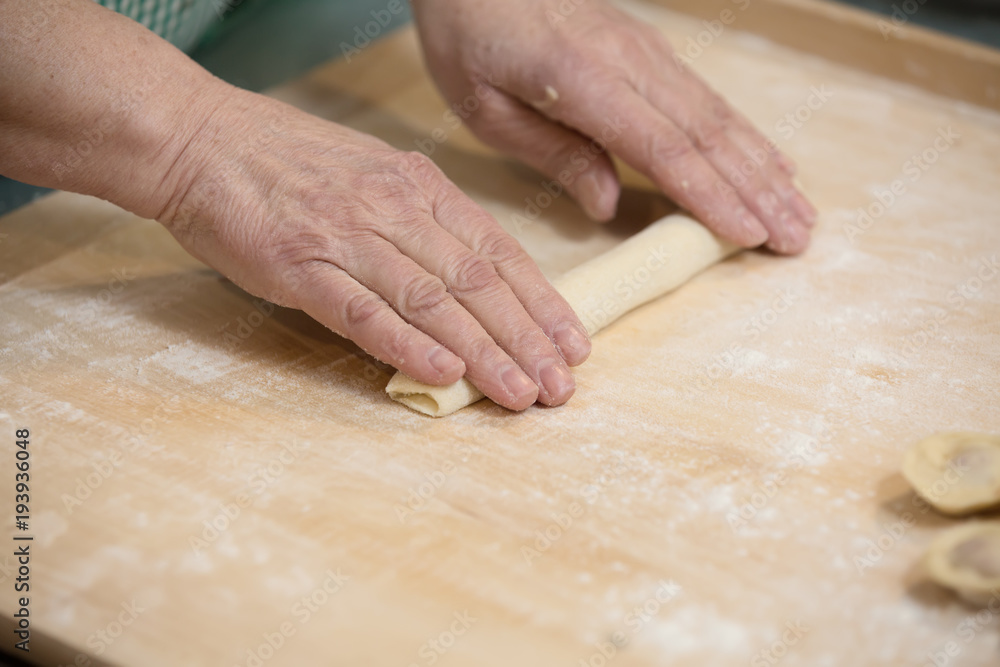 Dough made for modeling homemade ravioli, pelmeni or dumplings . Hands roll the dough on a wooden board. Home cooking, handmade.