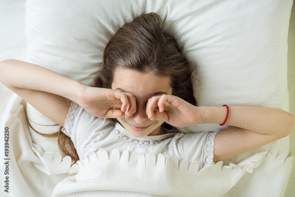 Girl child wakes up, rubs eyes. Lying on a pillow in bed, top view Girl child wakes up, rubs eyes. Lying on a pillow in bed, top view