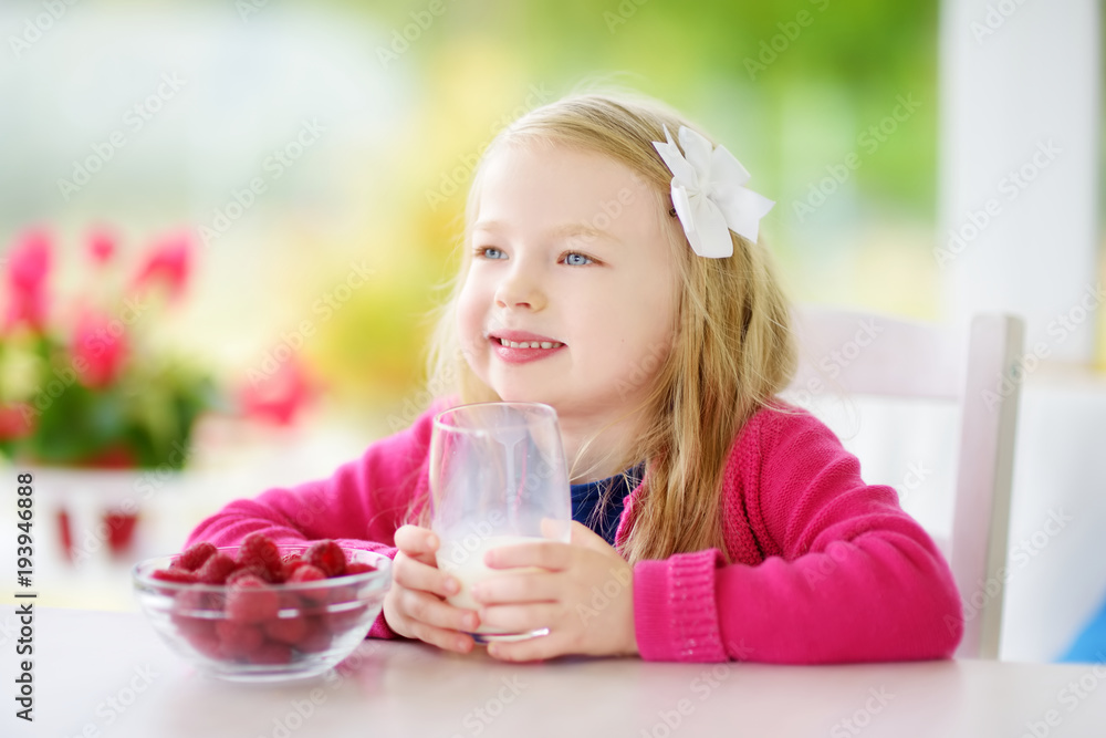 Pretty little girl eating raspberries and drinking milk at home. Cute child enjoying her healthy fresh organic fruits and berries. Pretty little girl eating raspberries and drinking milk at home. Cute child enjoying her healthy fresh organic fruits and berries.
