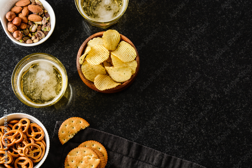 Light beer with a snack of chips, nuts and chesee on a black background. Light beer with a snack of chips, nuts and chesee on a black background.