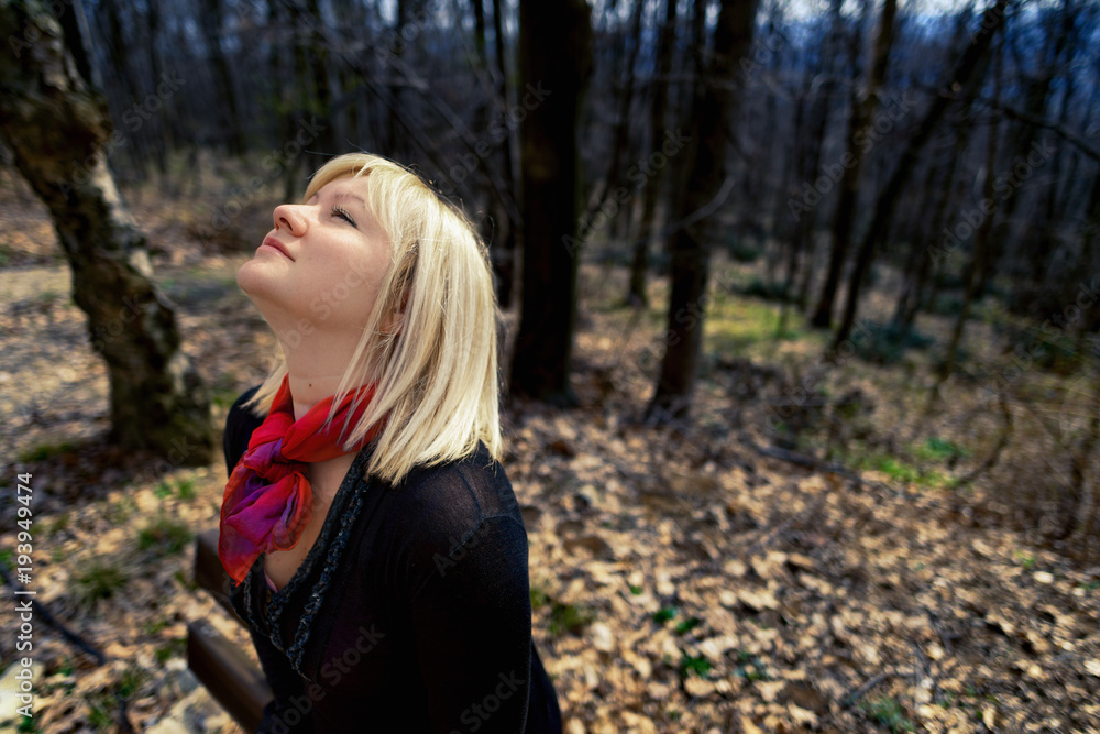 Blonde woman with red scarf and black shirt in the forest looking up the sky. Springtime, outdoor portrait.