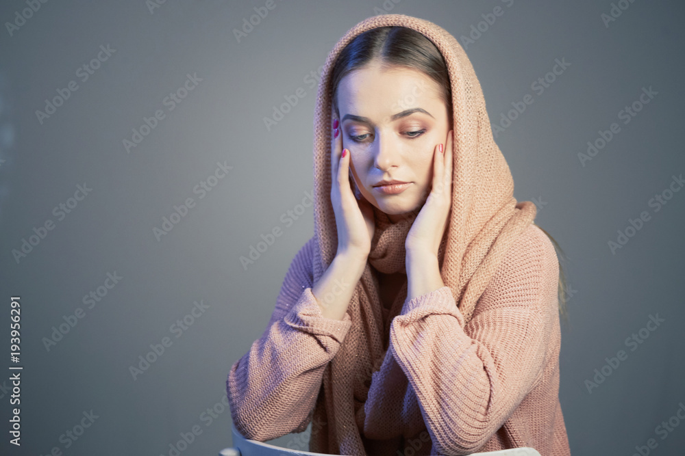 large emotional portrait of a beautiful girl in a knitted pink headscarf in the studio on a gray background. large emotional portrait of a beautiful girl in a knitted pink headscarf in the studio on a gray background.